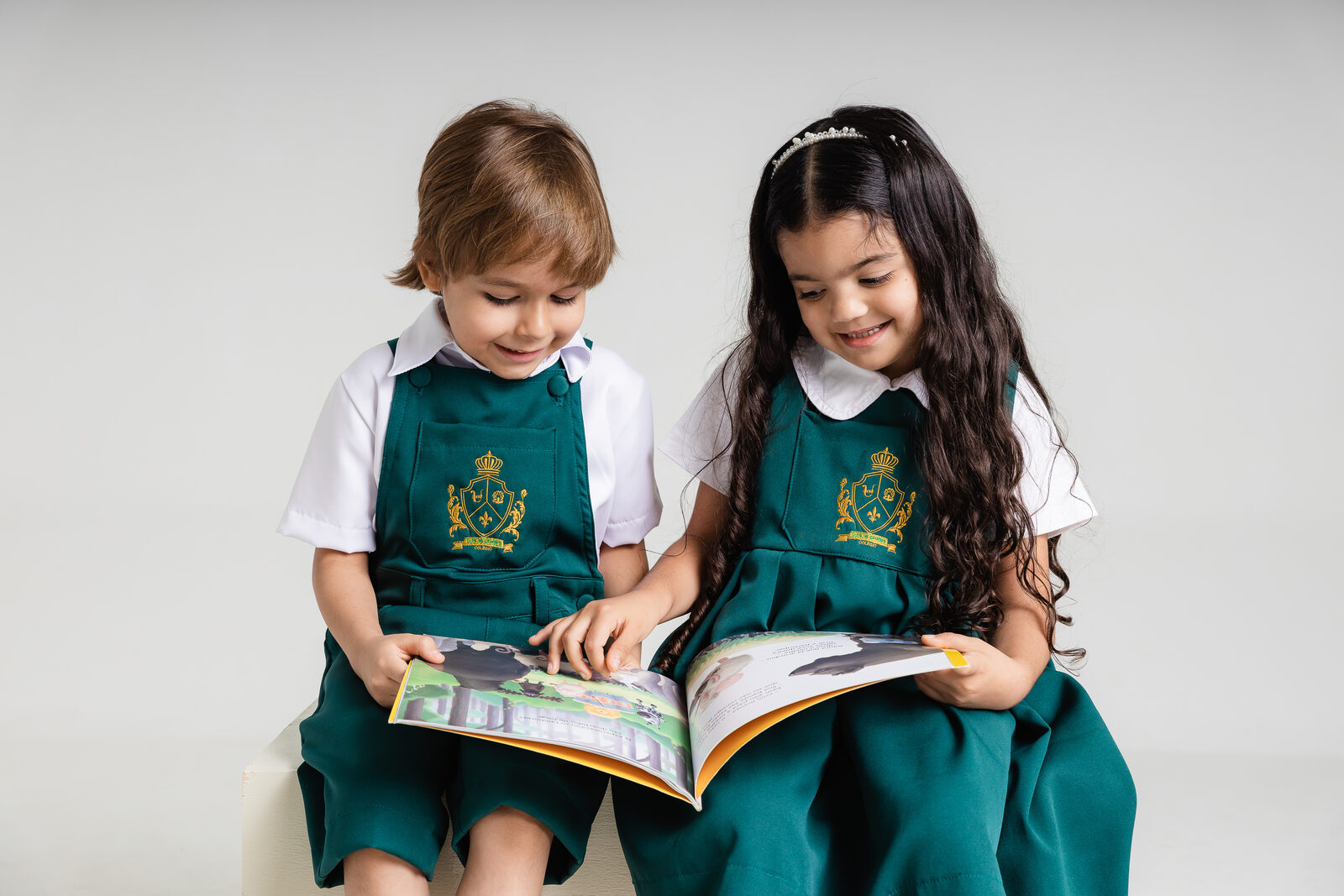 Alunos do Colégio Luís de Camões lendo um livro juntos, com o uniforme verde da escola